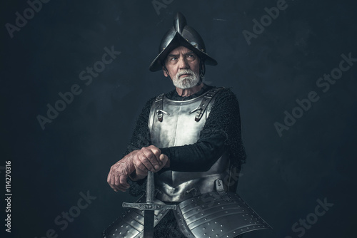 Plakat Rycerz z brodą w zbroi oparty na mieczu.