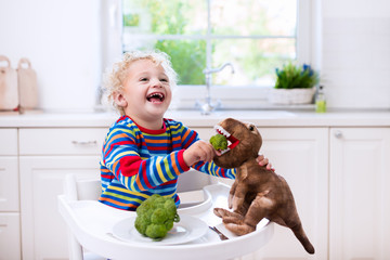 Wall Mural - Little boy feeding broccoli to toy dinosaur