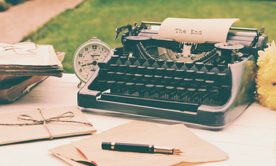 Wall Mural - Vintage black typewriter with  old books and flowers on wooden table, outdoors