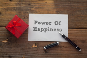 Power of Happiness written on paper with pen,red gift box and wooden background desk.