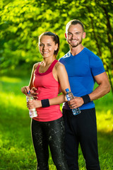 Man and woman drinking water from bottle after fitness sport exercise. Smiling couple with bottles of cold drink outdoors