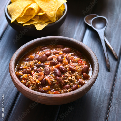 Fototapeta na szkło Rustykalna miska chili con carne z frytkami tortilli z tyłu, sfotografowana naturalnym światłem (Selective Focus, Focus w środku chili)