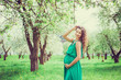 Pregnant beautiful woman in the apple orchard with a flower in her hair holding belly