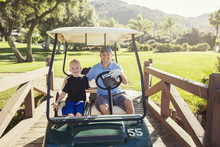 Father And Son Golfing Together On A Summer Day Riding In A Golf Cart Together