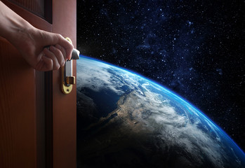 Wall Mural - hand opens empty room door to planet earth from the space. some