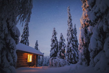 Cabin With Light On At Night In Snow, Finland