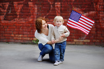 Wall Mural - Happy young woman with her toddler son holding american flag