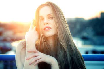 Wall Mural - Outdoor portrait of young pretty sexy woman with magic eyes posing at roof at the end of bright sunset. Lovely soft back light.