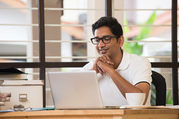 Wall Mural - casual indian man smiling and working at office