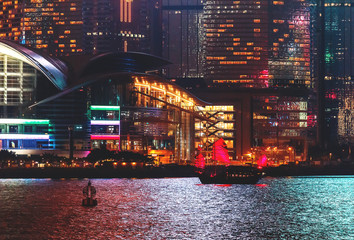 View over Hong-Kong, China, by night. Nighttime skyline with illuminated skyscrapers and the traditional junk boat.