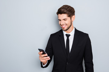 Cheerful young businessman in suit reading sms on smartphone