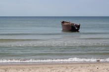 Old Wooden Maroon Fishing Boat At Anchor In Sea Near Sand Shore
