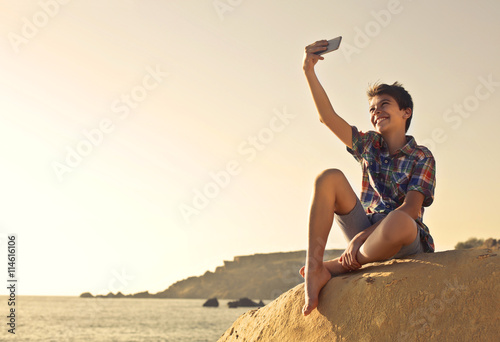 Fototapeta na szkło Młoda chłopiec robi selfie na plaży