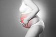 Caucasian pregnant woman in white lingerie with abdominal pain on gray studio background