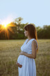 Pregnant woman in white dress watching the sunset outdoors