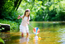 Cute Little Girl Playing In A River Catching Rubber Ducks With Her Scoop-net