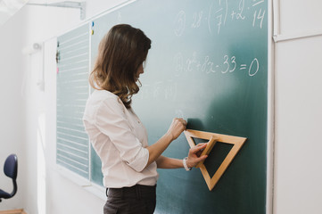 Smart student or teacher drawing mathematic formula at blackboard, dressed in university uniform, scribbled with chalk - formulas and drawing. Concept of intelligent and scientist woman