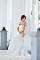 Beauty bride in bridal gown with bouquet and lace veil on the nature. Beautiful model girl in a white wedding dress. Female portrait in the park. Woman with hairstyle. Cute lady outdoors