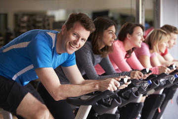 Man in a spinning class at a gym turning to smile at camera