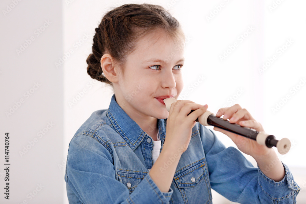 Little girl playing flute on light background