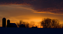 Silhouette Of Farm And Tree In Snow At Sunset