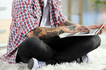 Canvas Print - Young man with tattoo using laptop on a floor at home