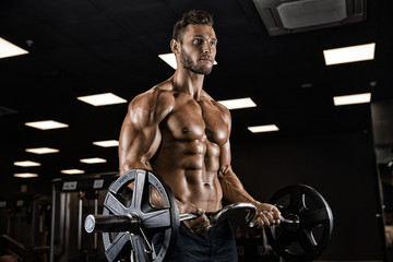 Muscular bodybuilder guy doing exercises with dumbbells in gym