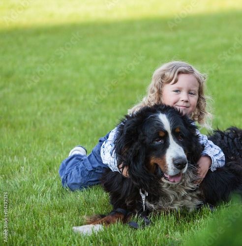 Happy Boy With Curly Blonde Hair Playing With Bernese Mountain Dog