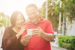© interstid - Happy senior Asian couple laughing tigether with mobile smartphone. Warm tone photo with sunlight