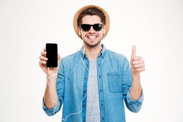 Wall Mural - Cheerful young man in earphones showing blank screen cell phone