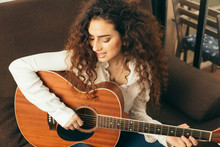 Girl Playing Guitar And Singing. Young Woman With Long Hair Studying Music At Home. She Plays Acoustic Guitar And Sing Alone At Home.