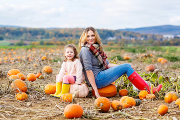 little kid girl and mother having fun on pumkin field