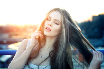 Wall Mural - Outdoor portrait of young pretty sexy woman with sensual lips posing at roof at the end of bright sunset. Lovely soft back light.