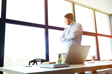 Wall Mural - Pensive young handsome man working on laptop while sitting at his working place