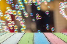 Empty Painted Wooden Table Or Plank With Bokeh Of Rainbow Soap Bubbles From The Bubble Blower On Background For Product Display.
