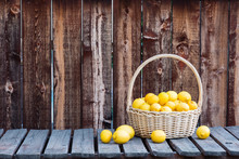 A Basket Of Many Lemons On A Rustic Plank Table And Background.
