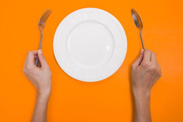 woman two hands hold a spoon and fork and white dish on yellow b