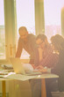 © astrosystem - Young group of people discussing business plans, with lap-tops, plans in a room lit by natural sunlight.