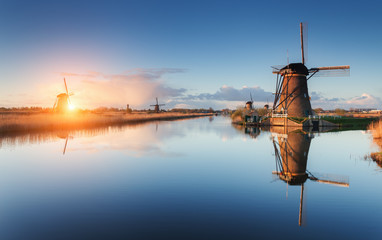 Beautiful traditional dutch windmills near the water channels with reflection in water at colorful sunrise in famous Kinderdijk, Netherlands