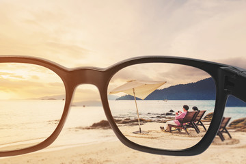 Wall Mural - Sunglasses with seascape and couple relaxing on the beach in sunset, vintage tone