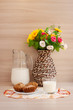 Завтрак из молока и кексов на вышитой салфетке. Плетеная ваза с цветами создает уют. 