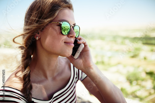 Fototapeta na szkło Fasonuje dziewczyny z telefonem komórkowym na naturze. Młoda atrakcyjna kobieta rozmawia przez telefon.