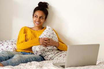 Wall Mural - Young woman sitting in bed with laptop and gazing away