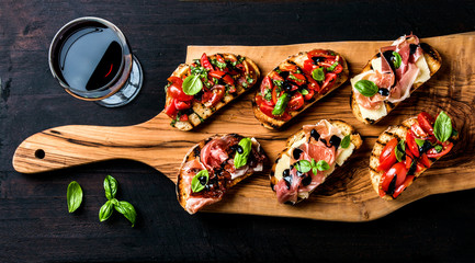 Poster - Brushetta set and glass of red wine. Small sandwiches with prosciutto, tomatoes, parmesan cheese, fresh basil, balsamic creme on rustic wooden board