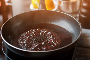 Wall Mural - Liquid boiling on frying pan. Black pan with dark liquid. Red wine for sweet sauce. High temperature needed for cooking.