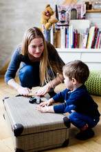 Mid Adult Woman Drumming On Suitcase With Baby Son On Floor