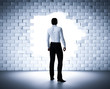 Businessman standing next to a hole in a brick wall. Light coming from outside