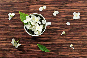 Poster - Cup of green tea leaves and jasmine flowers on wooden background