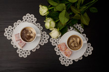 Top View Of Two Cups Of Coffee With Milk, Turkish Delight On A Saucer, White Roses. Black Background