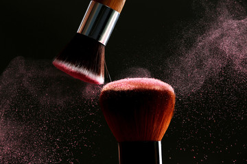 Makeup brushes with flying powder on black background